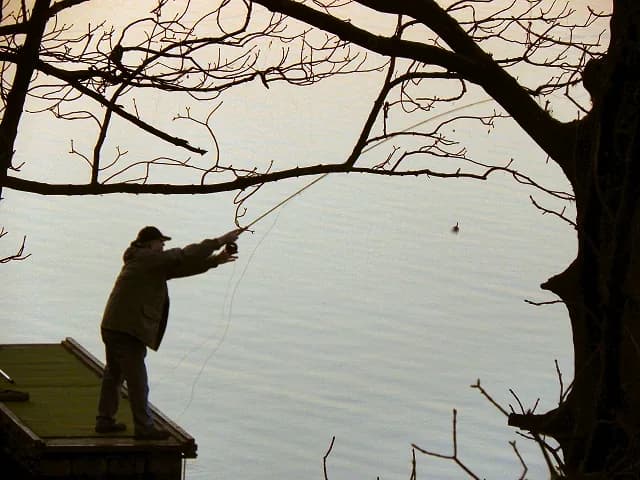 An angler fishing the bank of Wallsuches Reservoir, home of Curley's Trout Fishery, Horwich, Greater Manchester.