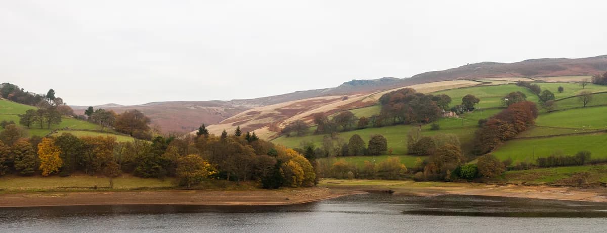 Wide autumn view of Ladybower Reservoir with wooded shoreline and Peak District moorland hills beyond