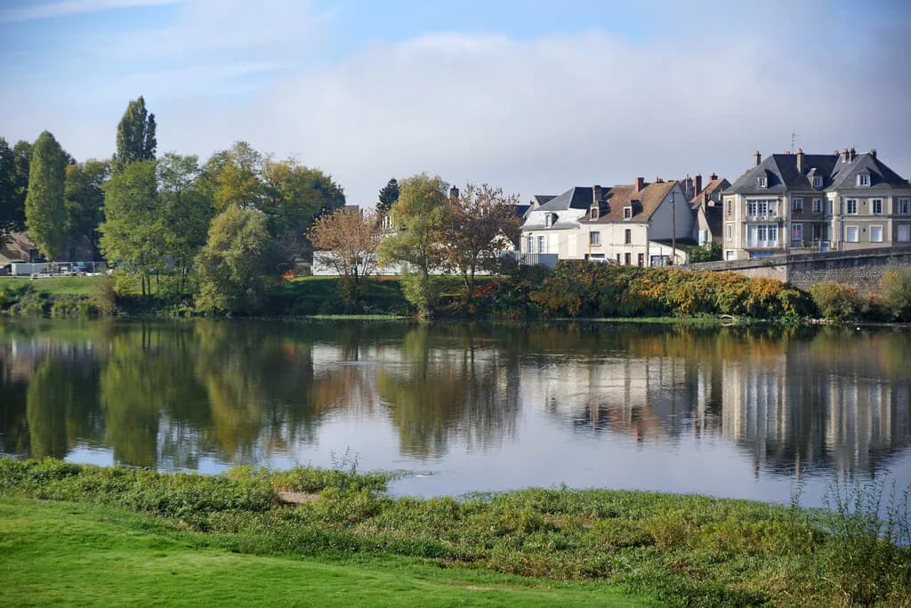 A calm, wide stretch of the Loire River with trees and a riverside town reflected in the still water.