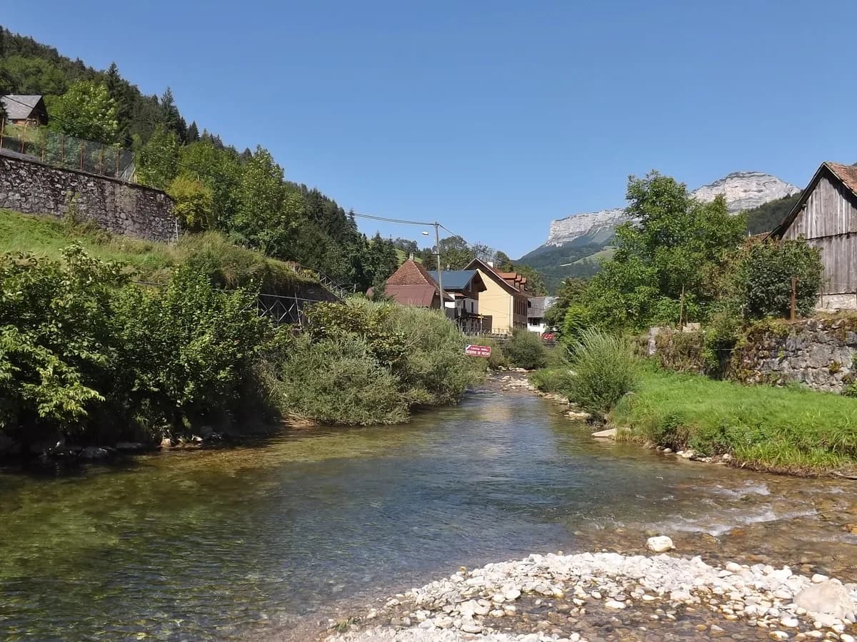 A clear mountain stream flowing through the village of Saint-Pierre-dEntremont with alpine peaks behind, on the Guiers river system
