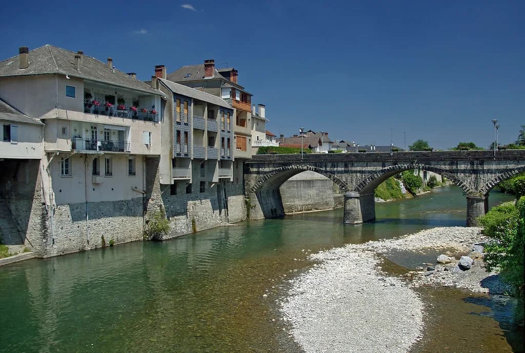 Clear green river flowing under an arched stone bridge past riverside houses in Mauléon-Licharre, France.