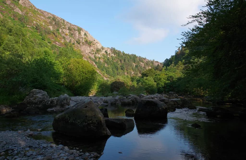 A rocky river gorge with large boulders in low, clear water, flanked by wooded hillsides, on the Afon Glaslyn near Aberglaslyn.