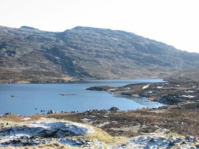 View across the still blue water of Llyn Eiddew Mawr towards a rocky hillside in Snowdonia, North Wales.