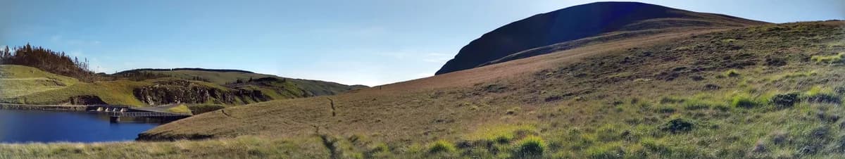 Panoramic view across Llyn Craig-y-Pistyll towards the peak of Craig-y-Pistyll, with the lake's dam visible, in the Welsh uplands.