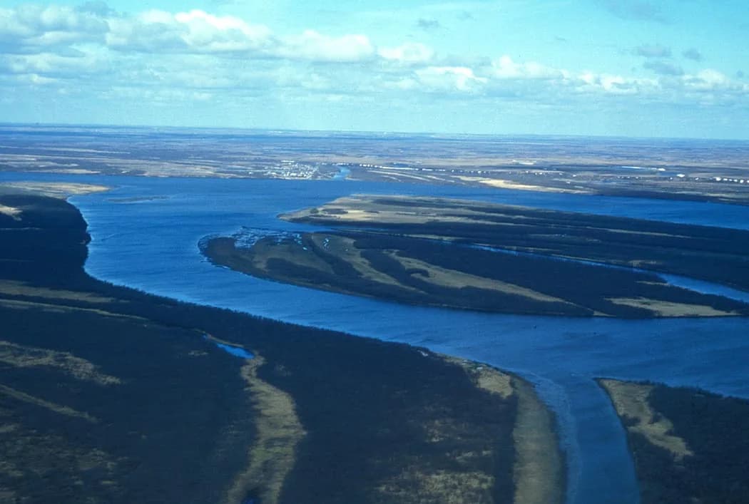 Aerial photograph of the Aniak River winding through tundra wetlands near its confluence with the Kuskokwim River in western Alaska, with the village of Aniak visible on the horizon.