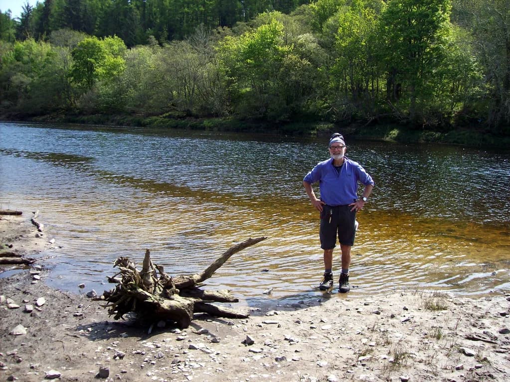 A wide, tree-lined stretch of the River Beauly with a gravel bank and a person standing in the shallows.