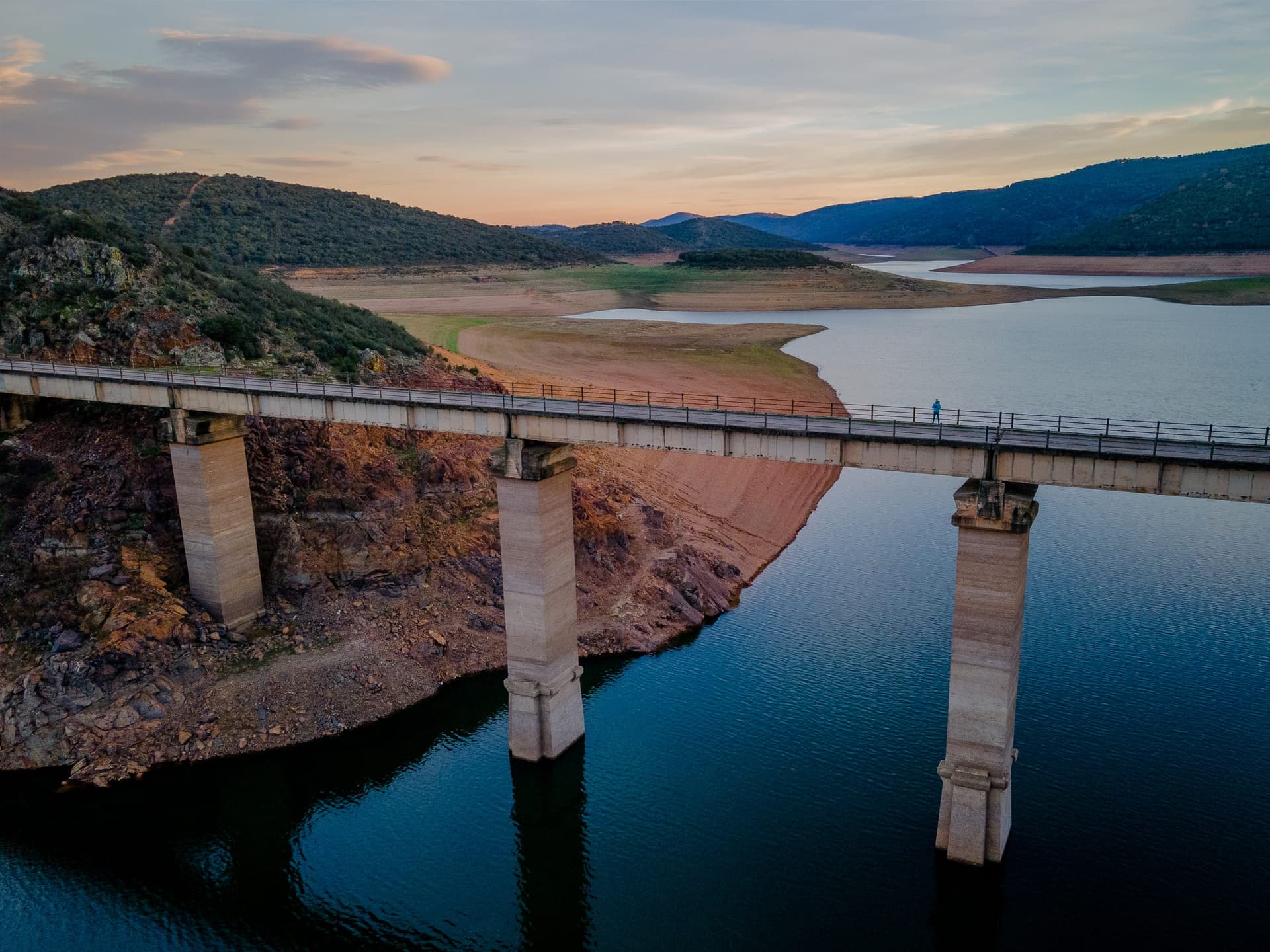 Ground-level photograph of Cíjara reservoir on the Guadiana with calm water reflecting oak woodland.