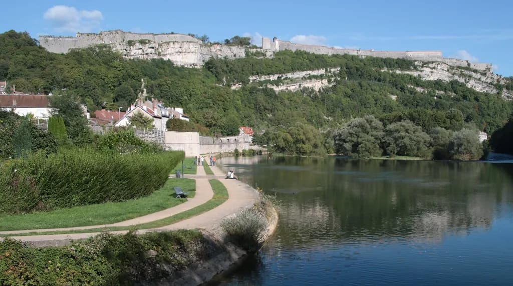 A wide, calm river bend with a riverside path and the historic citadel of Besançon on the hillside above.