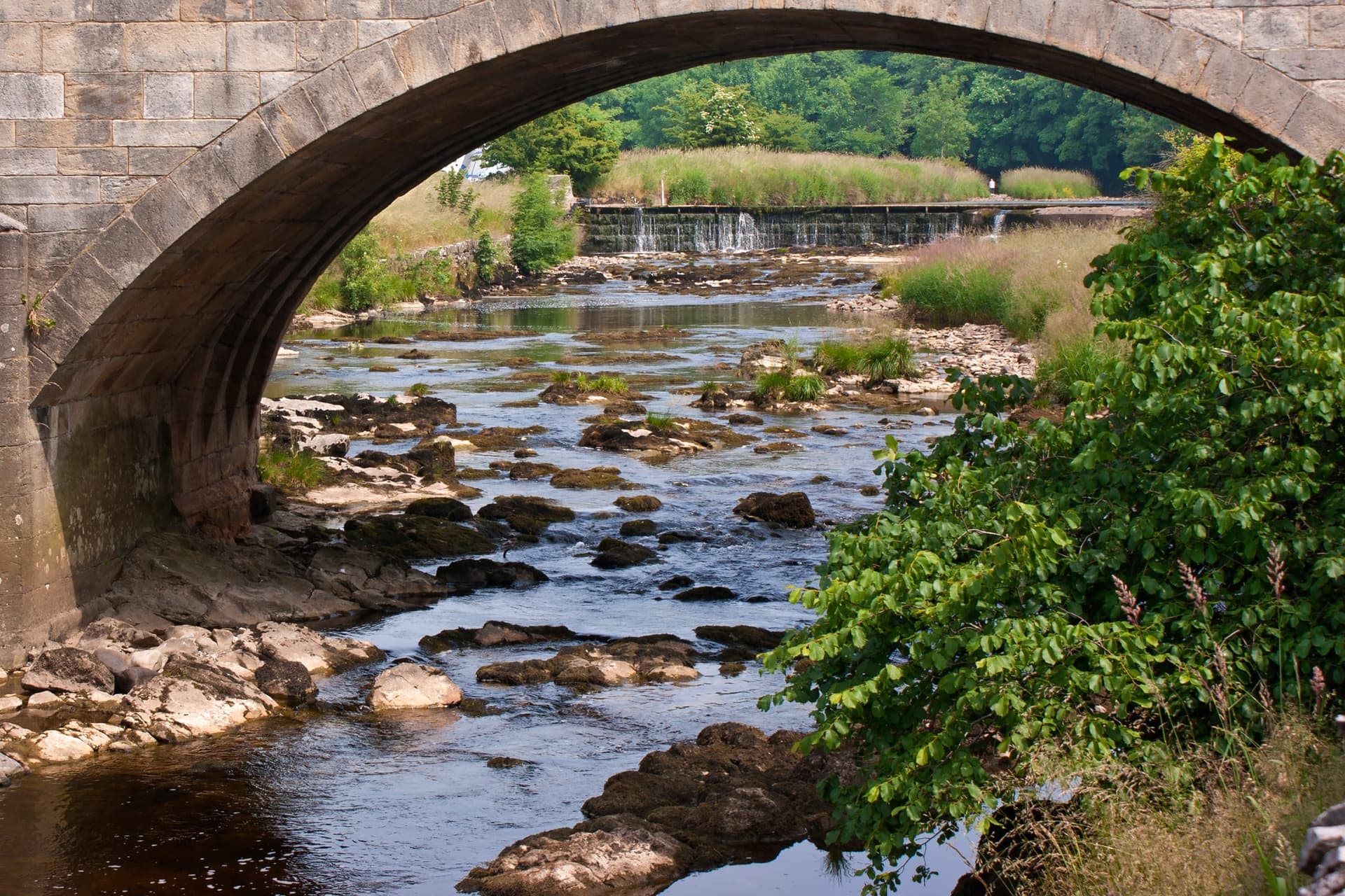 The River Ribble flowing through open countryside at Settle with a stony riverbed in low summer water.